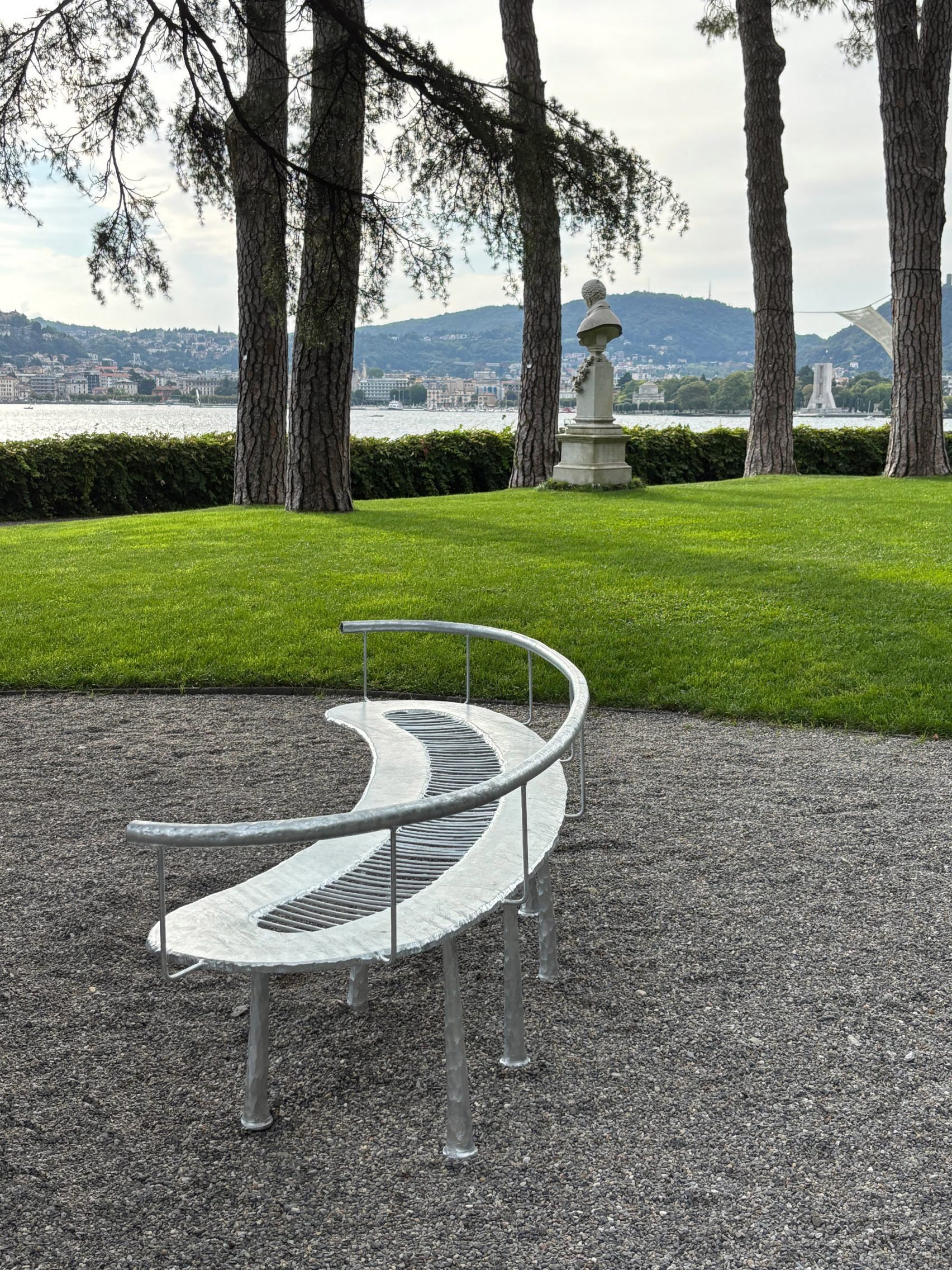 Steel bench on gravel in front of lawn with lake in background